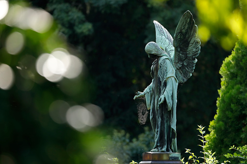 Weathered old copper angel statue with a spider web on a cemetery in Germany