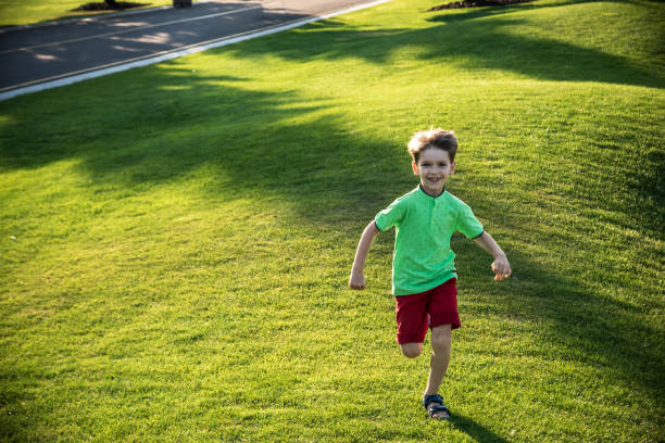 маленький мальчик работает на траве на огромном поле для гольфа - golf child sport humor стоковые фото и изображения