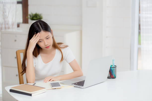 młoda azjatka ból głowy podczas pracy na laptopie z terminem na biurku w domu, kobieta biznesu z porażką wyczerpany i zmęczony, stres i zmartwiony, sfrustrowany i nieudany. - nieudany zdjęcia i obrazy z banku zdjęć
