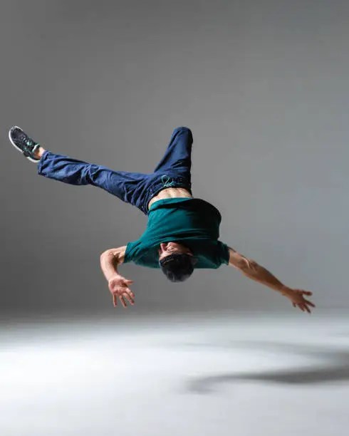 Stylish young guy breakdancer jumps dancing hip-hop isolated on gray background. Breakdance lessons. High quality photo