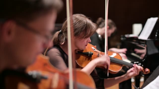 Focus on a young woman playing the violin with a string quartet and grand piano