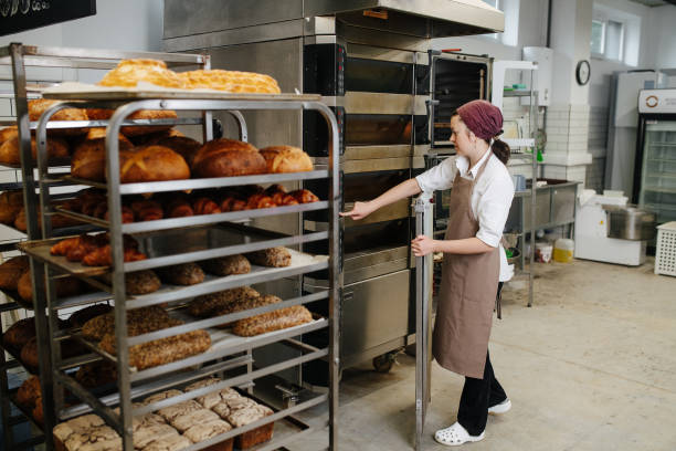 istock Working female baker standing next to a iron tray shelf with fresh bread 1273705734