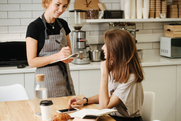 istock Enthusiastic waitress taking order from mature woman, sitting behind the table. 1273705738