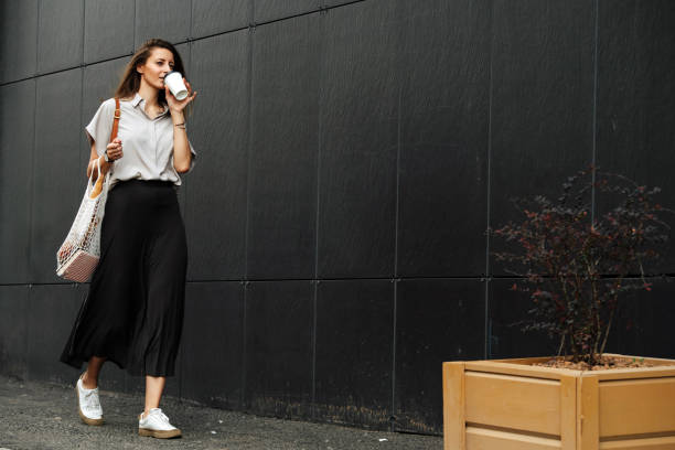 mujer de negocios madura caminando en el lado de una calle, bebiendo café - smelling bread bakery women fotografías e imágenes de stock