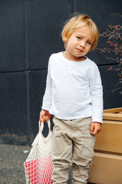 little boy with blond hair holding net bag, outdoors on the street - preschooler autumn beautiful blond hair imagens e fotografias de stock