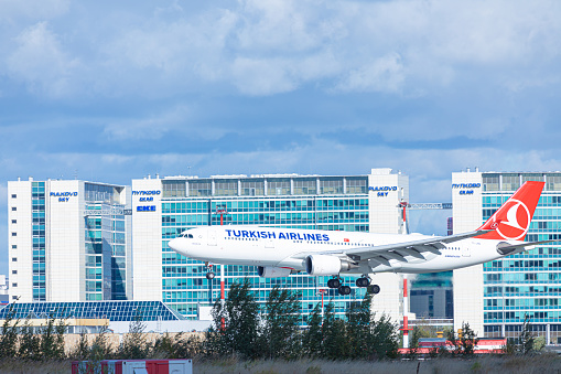 Pulkovo airport near Saint Petersburg/ Russia - September 19 2020: Airplane of turkish airlines company with chassis from the side landing or taking off on background of buildings and blue cloudy sky