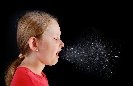Coughing girl on black background producing infectious droplets