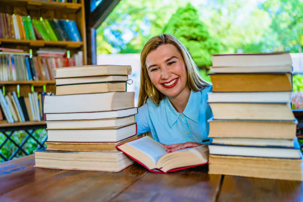 Young smiling woman reading among a pile of books in the open library
