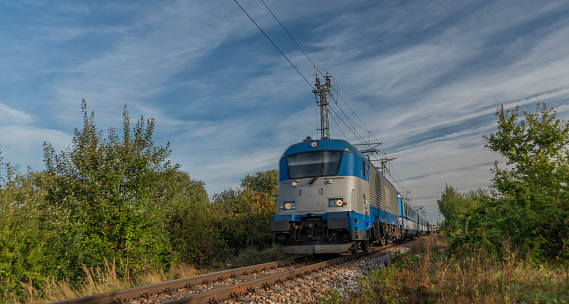 Blue electric engine and expres passenger train near Ceske Budejovice station in summer morning
