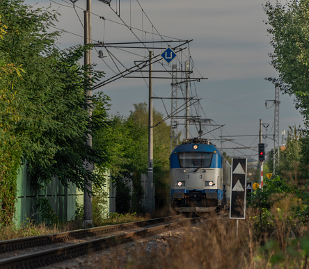 Blue electric engine and expres passenger train near Ceske Budejovice station in summer morning