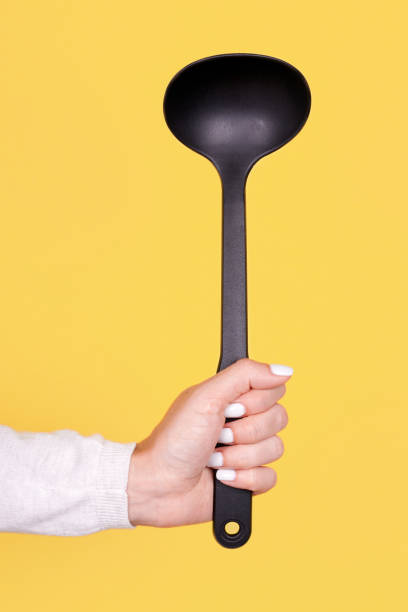 istock Black plasic ladle in hand, isolated on yellow background. 1273717578