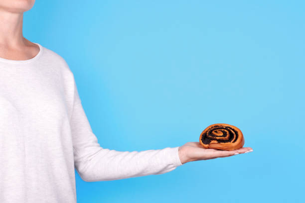 istock Handmade roll with poppy seed in hand, isolated on blue background. 1273719798