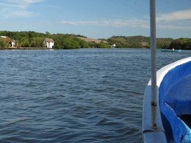 Veracruz, Mexico - 12th of January 2015. View on Laguna de Mandinga in Veracruz from a boat. In the foreground the front of a boat and water.  On the water a boat with a fisherman. In the background some houses and dunes with trees and a blue sky with some clouds.