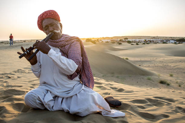 JAISALMER, INDIA - October 12, 2016: \nOld man wearing pagari (red turban) playing traditional music in the Thar desert for entertaining the tourists.