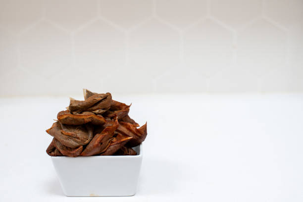 A pile of used tea bags in a square white dish with a white background