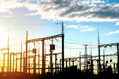 Distribution electric substation with high-voltage power lines and transformers at sunset, electric transmission tower