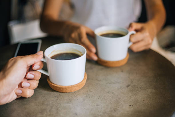 крупным планом женщина и мужчина, держащие чашки кофе на столе - coffee time стоковые фото и изображения