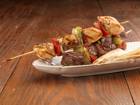 Grilled chicken and meat kebabs with vegetables with plate on wooden table.