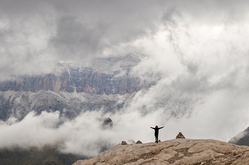 Silhouette of a woman standing on a rock against mountain ridges and clouds