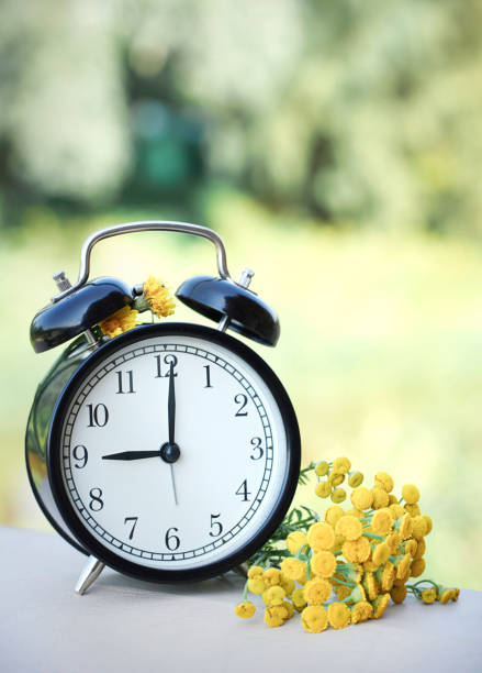 istock Blurred black retro alarm clock stands on the table against the Summer background 1273740389