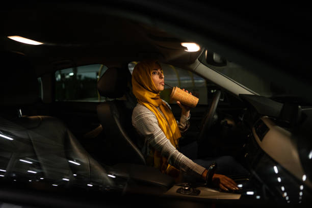 muslim female driver sitting in car and drinking coffee at night - car dashboard night driving imagens e fotografias de stock