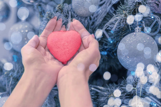 female hands hold heart on christmas tree. Blue christmas background