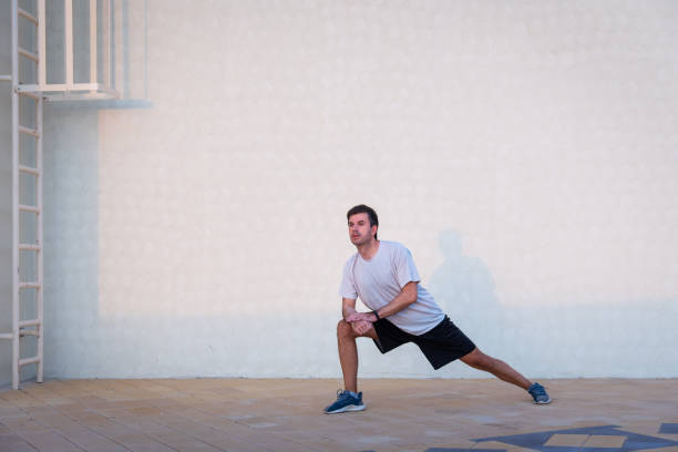 istock Man stretching before workout outdoors against clear white wall for copy space 1273748951