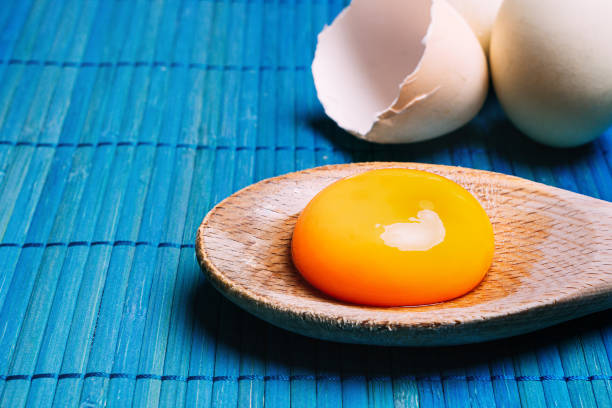 istock Raw egg yolk in a spoon next to eggs, on a blue background Ecological, traditional and healthy cooking 1273753500