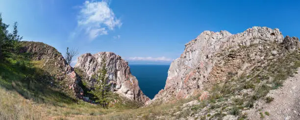 Cape Sagan-Khushun or Rocks Three brothers with red moss on the background of blue water and blue sky in summer time. Olkhon Island on Lake Baikal. Eastern Siberia, Russia. Panorama