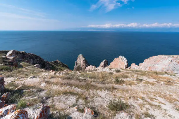 Cape Sagan-Khushun or Rocks Three brothers with red moss on the background of blue water and blue sky in summer time. Olkhon Island on Lake Baikal. Eastern Siberia, Russia