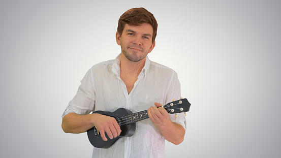 Medium shot. Front view. Smiling young man playing ukulele looking into the camera on gradient background. Professional shot in 4K resolution. 047. You can use it e.g. in your medical, commercial video, business, presentation, broadcast