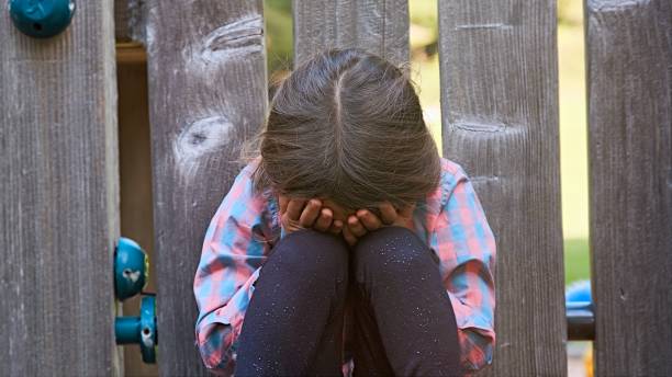 Menina criança chorando sentada no chão cobrindo seu rosto - foto de acervo