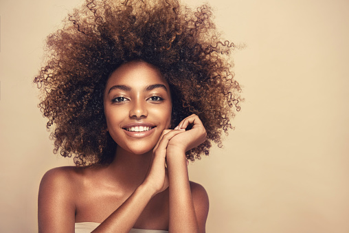 Portrait of perfectly looking brown haired young woman. Natural, dense afro hair on the head of young beautiful model, white toothy smile on her face. Girl with vibrant, melanin-rich skin tone. Look full of happiness.