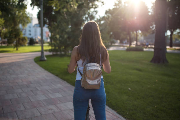istock Young woman with backpack riding electric scooter in a park 1273767505