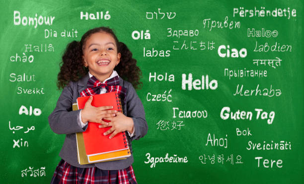 pequeña estudiante afroamericana con libro en la pizarra frontal - multilingual fotografías e imágenes de stock