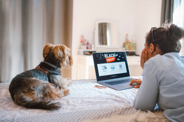 Woman Is Buying Electronics Online At Black Friday Discounts Woman is buying electronics online at Black Friday while relaxing at the bed with her dog black friday stock pictures, royalty-free photos & images