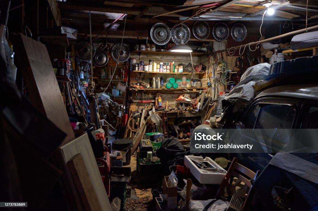 Super Cluttered Garage full of tools and materials An old garage in a barn with heels of containers and metal and scrap alongside a vintage old car. Garage Stock Photo