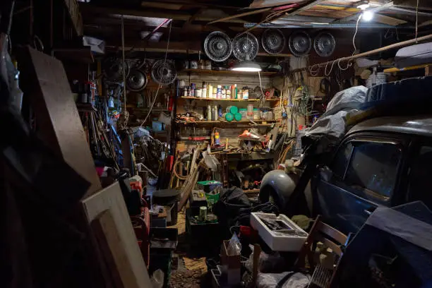An old garage in a barn with heels of containers and metal and scrap alongside a vintage old car.