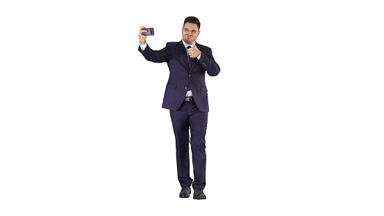 Full length shot. Handsome man in suit taking a selfie while walking on white background. Professional shot in 4K resolution. 014. You can use it e.g. in your commercial video, business, presentation, broadcast