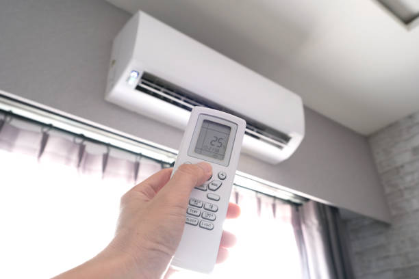 Man's hand using remote control open The air conditioner is cooled to 25 degrees Celsius in his bedroom. Health concepts and energy savings stock photo