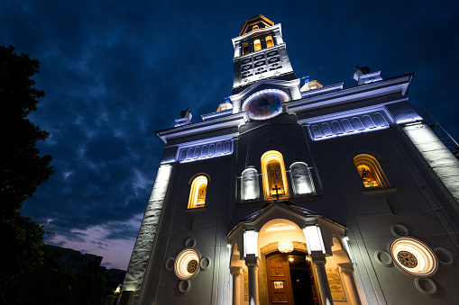 Color image depicting the exterior architecture of an orthodox church in the Transylvania region of Romania. It is night and the church is beautifully illuminated with blue and gold light.