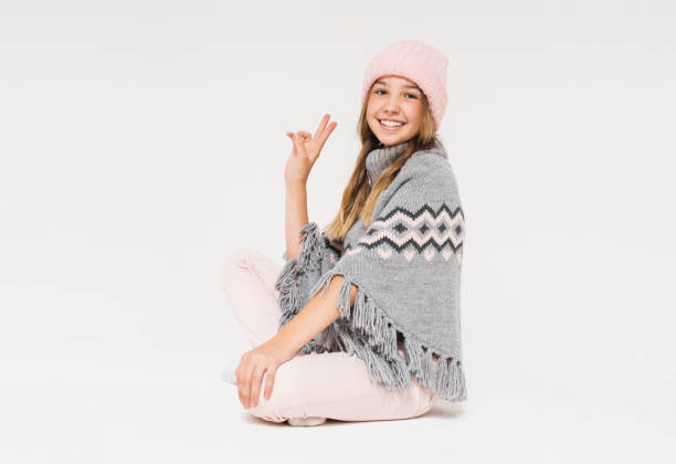 Cute smiling teenage girl in pink knitted hat and cozy gray poncho isolated on the white background Cute smiling teenage girl in pink knitted hat and cozy gray poncho isolated on white background kids winter fashion stock pictures, royalty-free photos & images