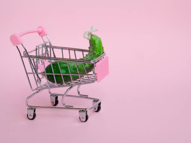Small shopping cart with big cucumber on pink background Small grocery cart with big unusual cucumber on pink background unusual basket stock pictures, royalty-free photos & images