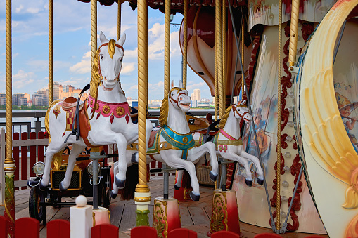 A happy mother and son are riding on a carousel together, smiling and having fun at an amusement park.  The boy holds two thumbs up.