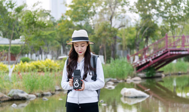 Woman taking photos with a vintage camera in park.
