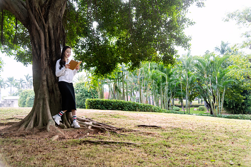 Young woman reading book under a tree.
