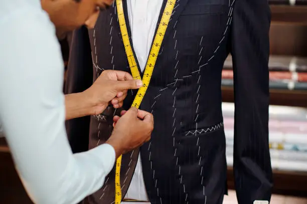 Profesional tailor making bespoke suit for client in his modern stidui