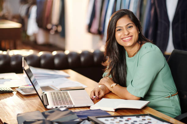 Happy young Indian atelier owner Portrait of happy young Indian atelier owner working on laptop atelier fashion photos stock pictures, royalty-free photos & images