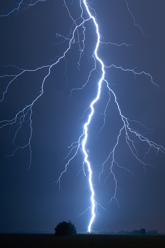 huge thunderbolt, lightning during thunderstorm on a summer evening over rural landscape striking in a tree