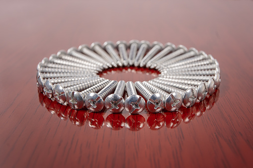 A group of silver screws arranged in a circle on a surface with wooden finish
